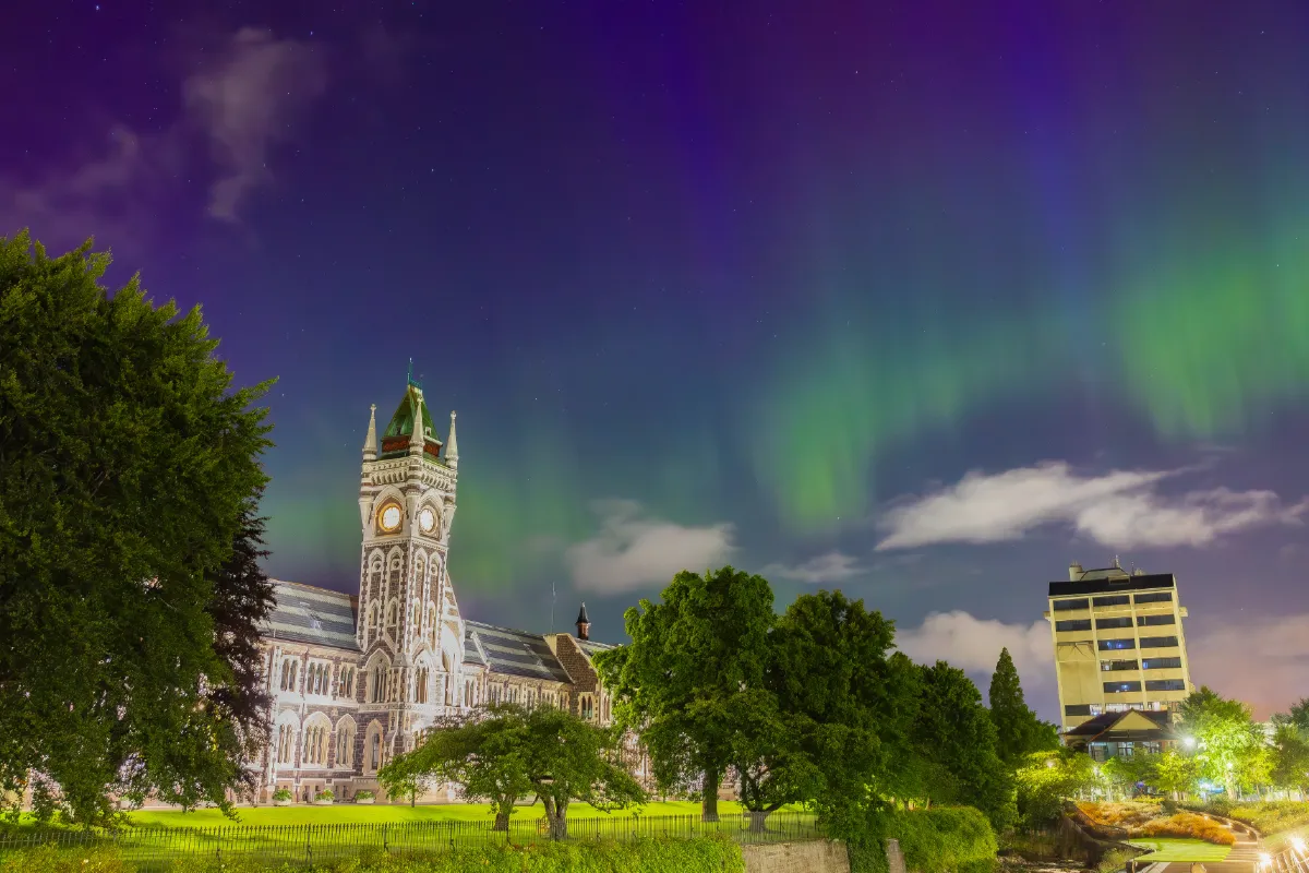 The University of Otago clocktower building at night, illuminated by the vibrant green and purple glow of the Aurora Australis.