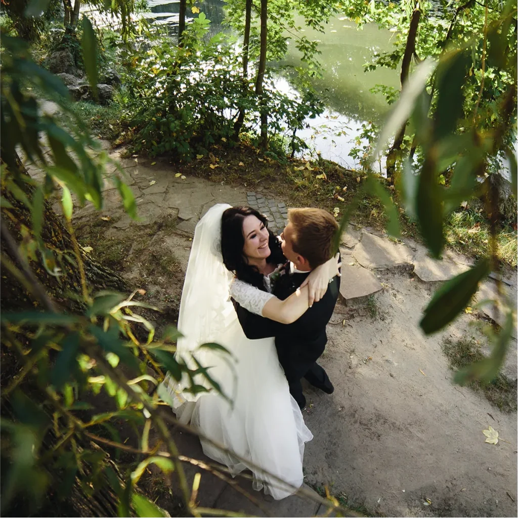 High-angle shot of a bride and groom embracing on a stone path by a lake.
