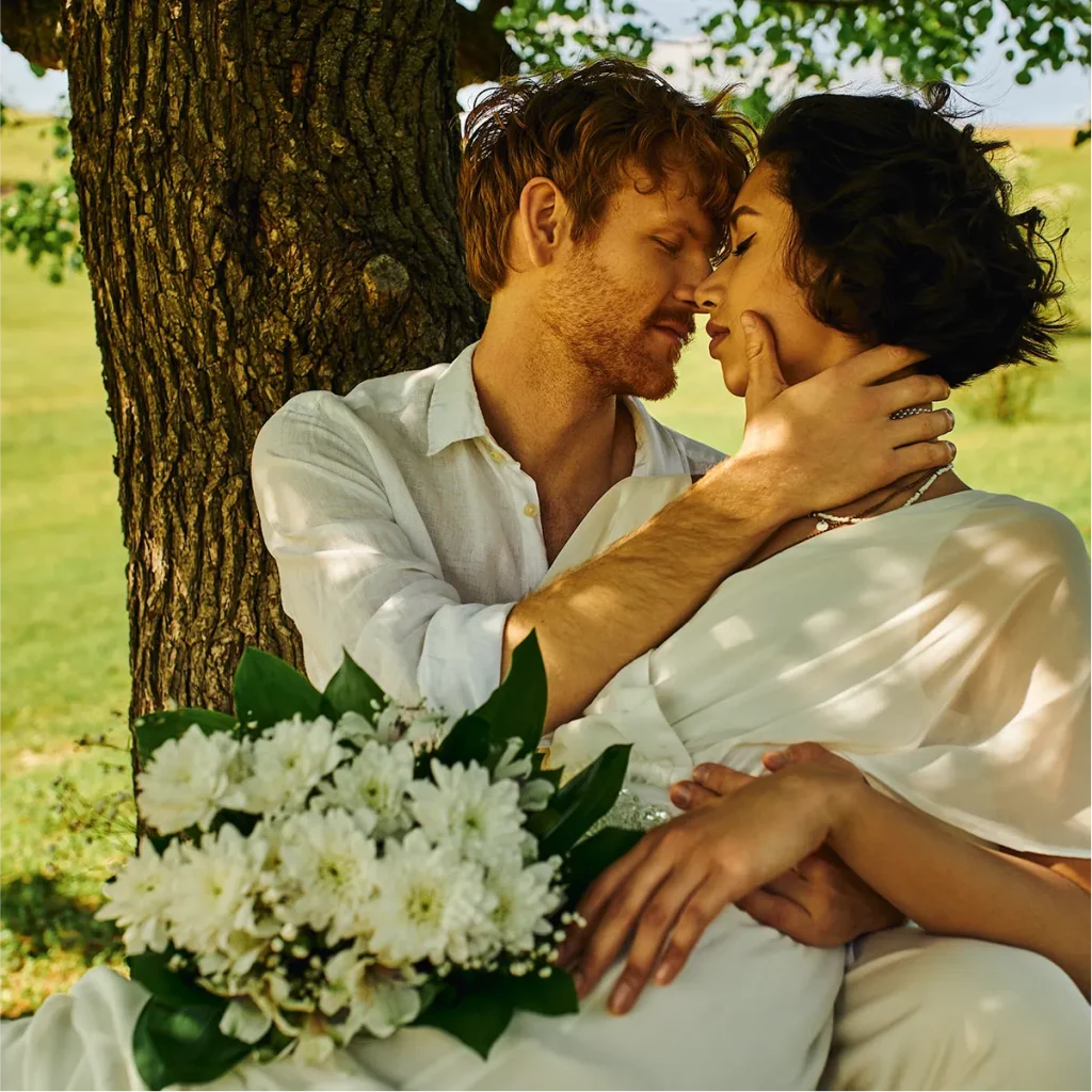 An intimate portrait of a couple sitting against a tree, the groom holding the bride's face.