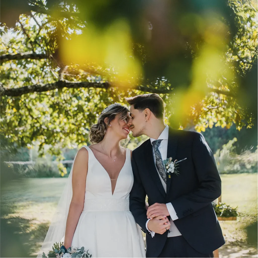 A wedding couple sharing a quiet moment under a sun-drenched tree in a garden setting.